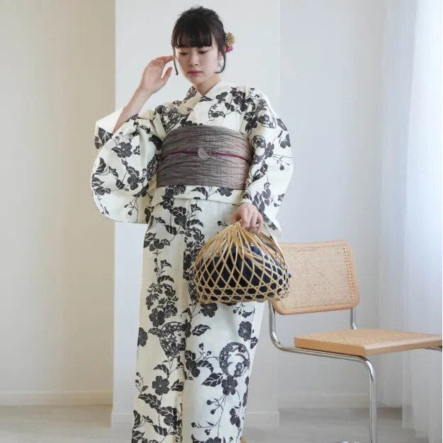 Woman wearing a floral kimono holding a netted bag in a minimalistic room.