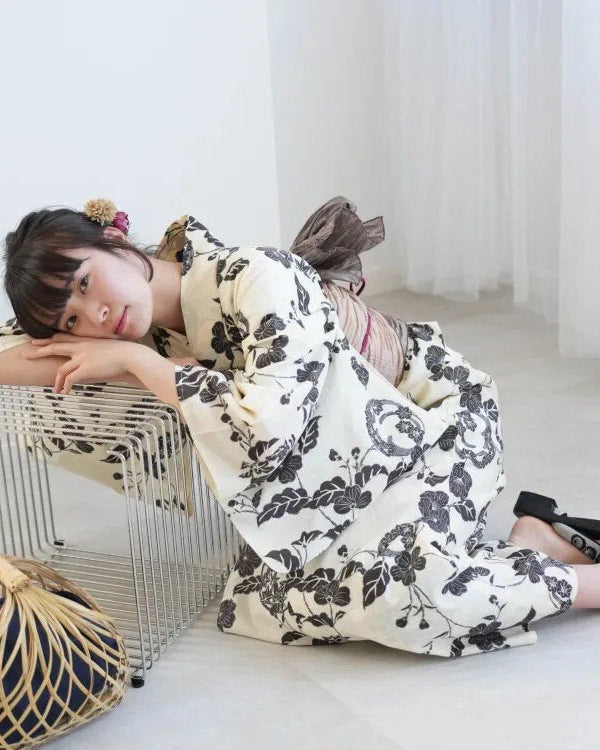 Woman in a floral kimono sitting on a white floor with a white curtain in the background