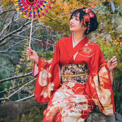 Woman in a red kimono with floral accessories standing in a natural setting.